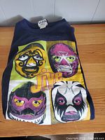 Front view of folded navy blue sweater showing large colorful graphic print of four wrestler masks with 'Fresh Jive' logo overlay.
