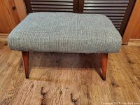 Full view of the footstool showing the padded upholstered top with a textured checkered fabric.