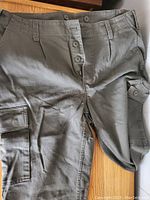 Close-up front view of olive green moleskin pants showing button fly and side pocket with flap.