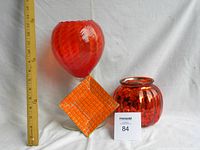 Photo showing all three items together with a ruler for scale: a red swirled glass goblet, a mottled red round vase, and an orange square dish.
