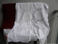 White tablecloth with circular crochet patterns and scalloped edged detail spread out, showcasing size and design.