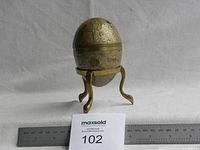 Front view showing the brass decorative egg placed on the brass stand, with ruler for scale.