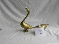 Front side view of taller brass goose figurine with arched neck and open beak, showing scale with a ruler