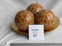 Three ceramic decorative balls on a large gold-colored plate with a ruler below showing scale.