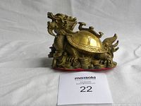 Side view showing the dragon-like head, detailed shell with hexagonal pattern, and various coins beneath the turtle figurine.