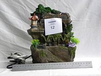 Front view of the Chinese-themed circulating desk fountain showing stone arch, pavilion, plants, and power cord with ruler for scale.