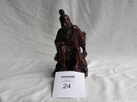 Front view of the dark reddish-brown wooden figurine of a seated elderly man with traditional hairstyle, beard, and robes.