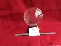 Crystal ball on wooden pedestal with a ruler in front to show scale, placed on red fabric background.
