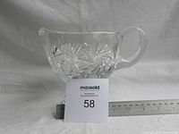 Front view of the heavy solid crystal gravy boat showing cut starburst and fan patterns, handle, and pedestal base with ruler for scale.