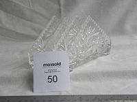 Photo showing three clear crystal napkin holders with intricate cut-glass designs displayed on a cloth background with a measurement scale.