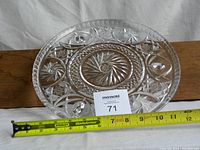 Top-down view of the clear crystal platter showing intricate pinwheel and starburst cut design with a measuring tape next to it indicating approximately 10 inches in diameter.