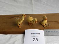 Three ceramic duckling figurines positioned on a wooden board with a metal ruler showing scale in front