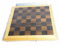 Top-down image of the 15x15 inch chess/checker board showing alternating dark Macassar ebony and lighter Bloodwood squares framed with oak trim.