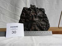 Front view of grotesque face carving with ruler showing size (about 7 inches wide).