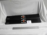 Two black rubber bar drain racks sized with a ruler for scale on a white background