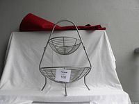 Front view of the two-tier metal wire basket with small basket suspended above larger basket. Ruler in front shows approximate size.