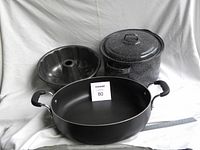 Photo shows three items on a white backdrop: black non-stick fry pan with two handles, black Bundt cake pan with fluted sides, and small black granite ware pot with white speckled pattern and lid.