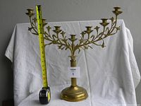 Close-up view showing height measurement of candelabra using a measuring tape held next to the item, measuring approximately 17 inches tall.