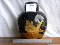 Front view of large black ceramic ginger jar with gold fish design, ruler placed for size scale.