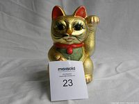 Front view of the golden ceramic lucky cat coin bank showing its face, raised paw, and part of the red collar.