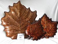 Three ceramic maple leaf shaped dishes: one large cream colored dish and two smaller brown-orange dishes with leaf vein detailing.