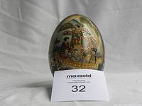 Front view of Satsuma egg showing a traditional Japanese scene with figures on a boat, with gold detailing and a ruler for scale.