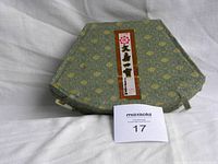 Closed hexagonal green fabric case with yellow pattern and Chinese label on top, ruler for scale.