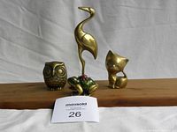 Photo showing all four brass figurines together on a wooden surface with a ruler for scale: bird, owl, cat, frog.