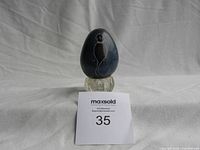 Full view of soapstone egg on small glass stand with MaxSold lot tag in front