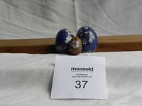 Three cloisonné eggs arranged in a row with lot number card in front on white fabric background.