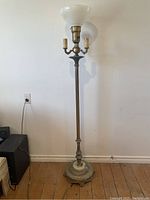 Full view of the antique brass floor lamp showing tall slender body, ornate decorative base, milk glass bowl shade, two smaller candelabra candle sleeve holders under main shade.