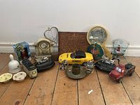 Photo showing assorted antique toys and decorative items on wooden floor including yellow convertible car, red toy truck, miniature train, clock with key, small ceramic dishes, and other items.