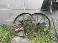Two rusted antique metal wagon wheels leaning outdoors against a cinder block wall, showing spokes and central hubs.