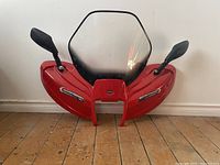 Front view of red ATV windshield showing integrated mirrors and clear windshield panel.