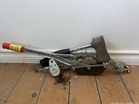 Come-along winch and hatchet on wooden floor next to white wall