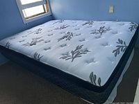 Full view of double mattress showing white quilted top with floral design and dark blue supportive base.
