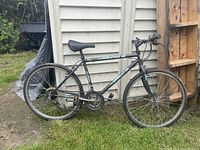 Side view of the entire Barletta All Pro 18 men's mountain bike against a white building, showing tires, frame, handlebars, and saddle.