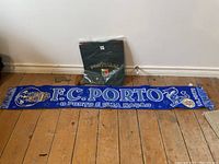 Photo showing the black Portugal T-shirt folded in packaging and the blue F.C. Porto scarf laid out on wooden floor.