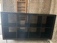 Front view of black shelving unit with 8 square compartments, showing the full rectangular shape and open storage design.