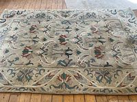 Overall view of the rectangular wool carpet showing floral and vine pattern with multiple colors on neutral beige background laid on wooden floor.