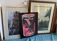 Three framed pieces of artwork displayed next to each other on a blue cloth surface. Middle item is The Rolling Stones Goats Head Soup poster. Left artwork shows a totem pole. Right artwork shows a waterfall scene.