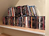 Wide view of multiple DVD and Blu-ray cases stacked on shelf including various movie titles.