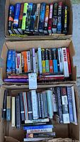 Three open boxes filled with hardcover books in a variety of titles and authors, showing overall quantity and condition.
