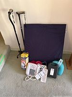 Full view of the lot with canes, foam pillow, wrist brace in packaging, photodial phones, heated neck pillow, exercise ball, and visible cords and instruction manuals.