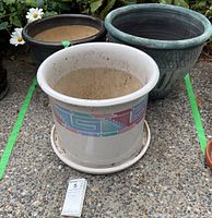 Three ceramic plant pots positioned outdoors on concrete, showing different designs and colors.