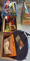 Overview of three boxes containing children's toys and puzzles including colorful Fisher Price toys, boxed puzzles and plastic bowling pins.