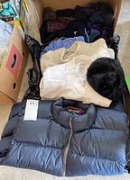 Box with mixed clothing including Marmot vest, jackets, and other folded garments.