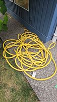 Yellow coiled rubber garden hose lying on the ground near a building exterior.