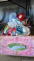 Pink treasure chest box with princess-themed oval panel and kids dress up clothes piled on top