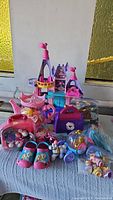 Photo of princess castle playset with various toys, Barbie clothes, and small accessories arranged on cloth surface